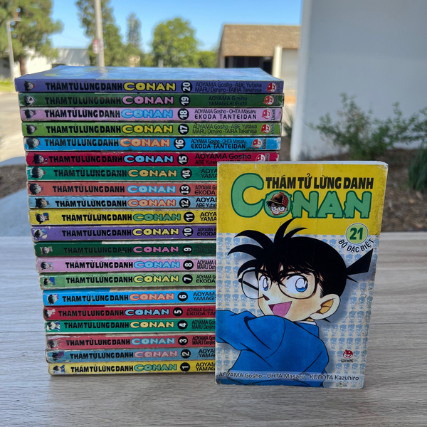 Stack of 'Conan' manga books with a single book cover displayed in front on a wooden surface.